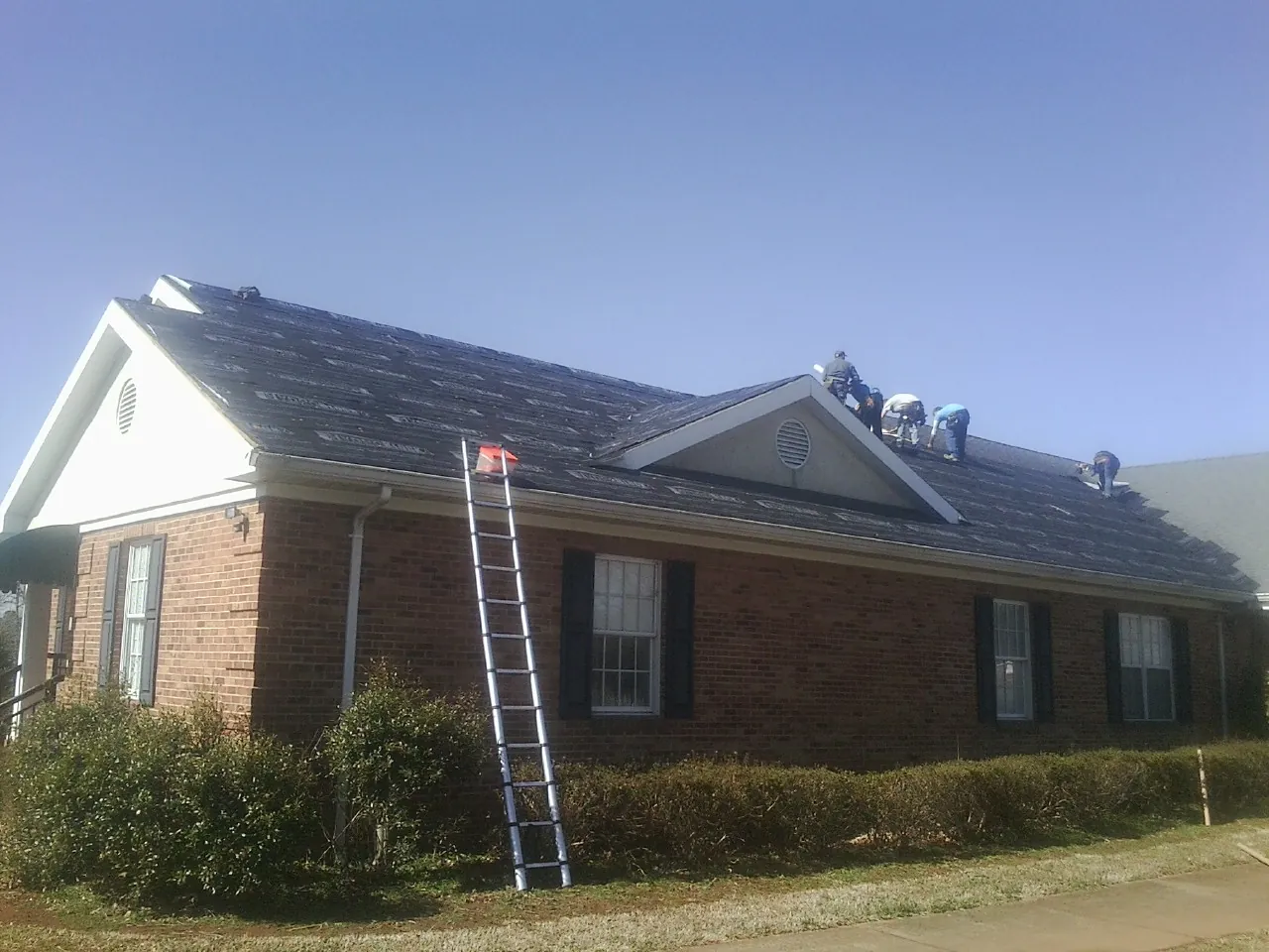 Crew tearing shingles off a brick ranch roof with a ladder set — Emergency Roof Repair work by our crew in Pevely