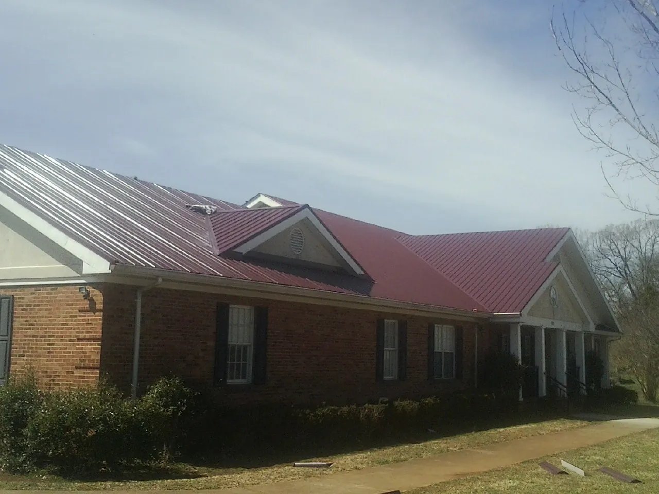 Red metal roof with gabled entries on a long brick building, from a Hail Damage Roof Repair job in Pevely