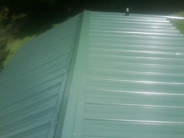 New green metal panels meeting at the ridge of a roof — Flat Roof Repair work by our crew in Pevely
