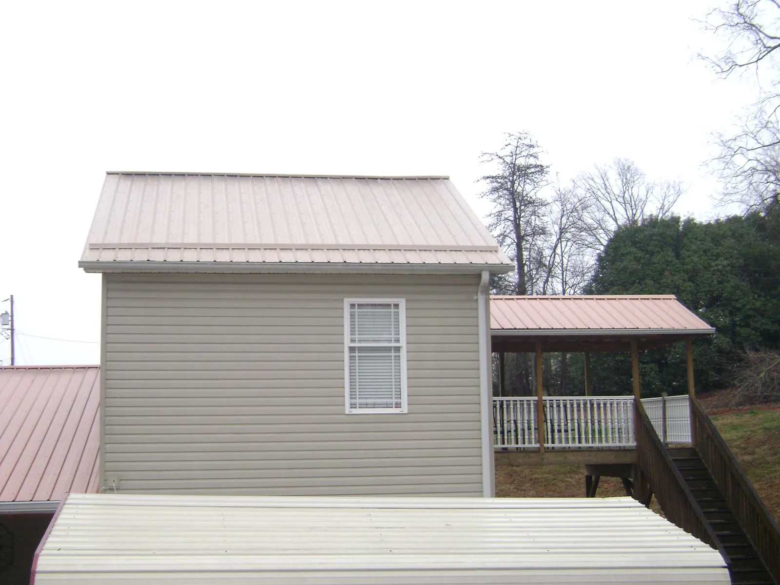 Tan metal roofs on a two story addition and attached porch, from a Roof Replacement job in Pevely